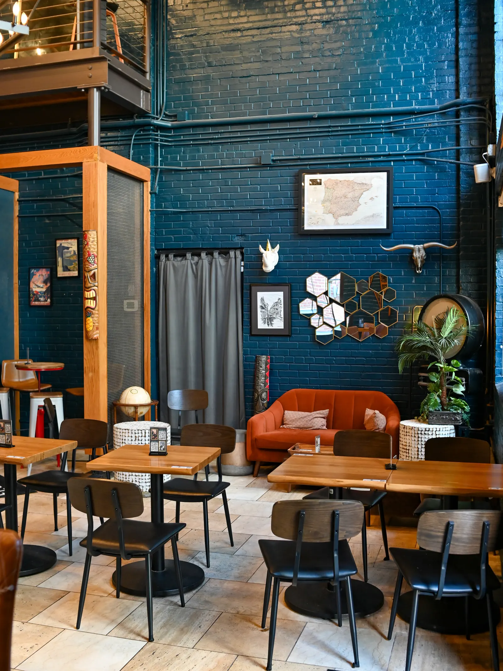 Elsewhere lounge with an orange sofa, blue brick walls, and tables for gathering